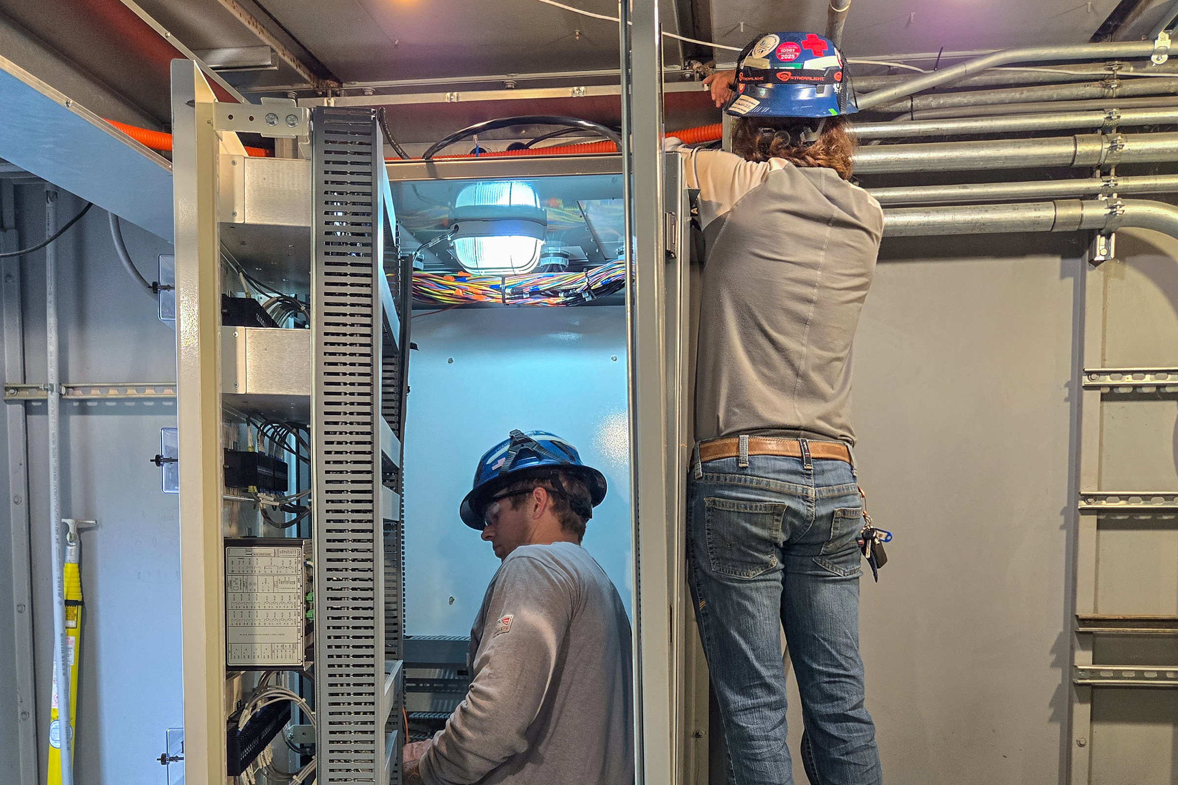 Two electrical technicians installing a direct transfer trip scheme into an electrical cabinet.